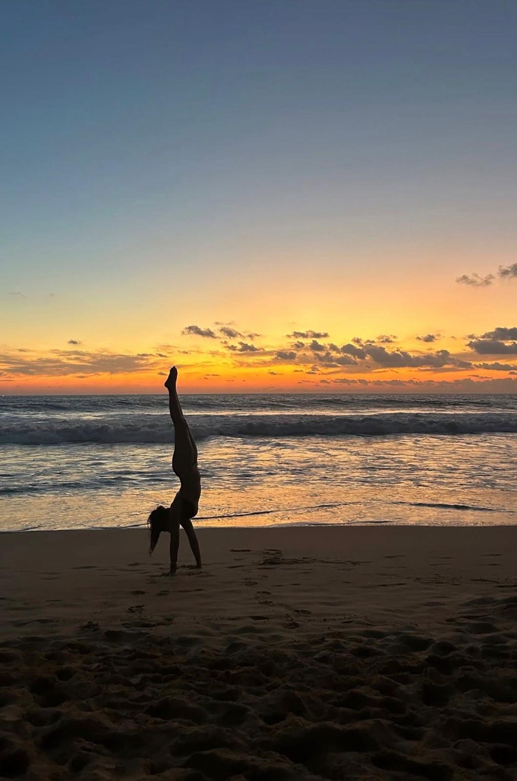 Pallavi balancing in a handstand on a beach at sunset
